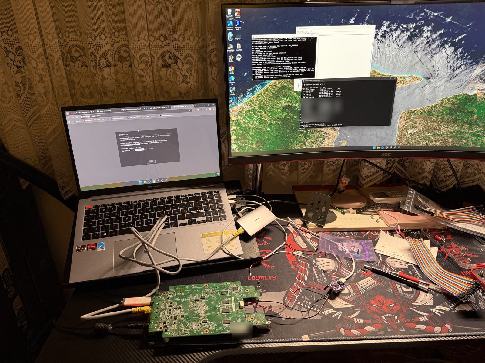 Laptop showing the WD Safe Mode firmware upload page next to the bare PR2100 board wired to a USB serial adapter